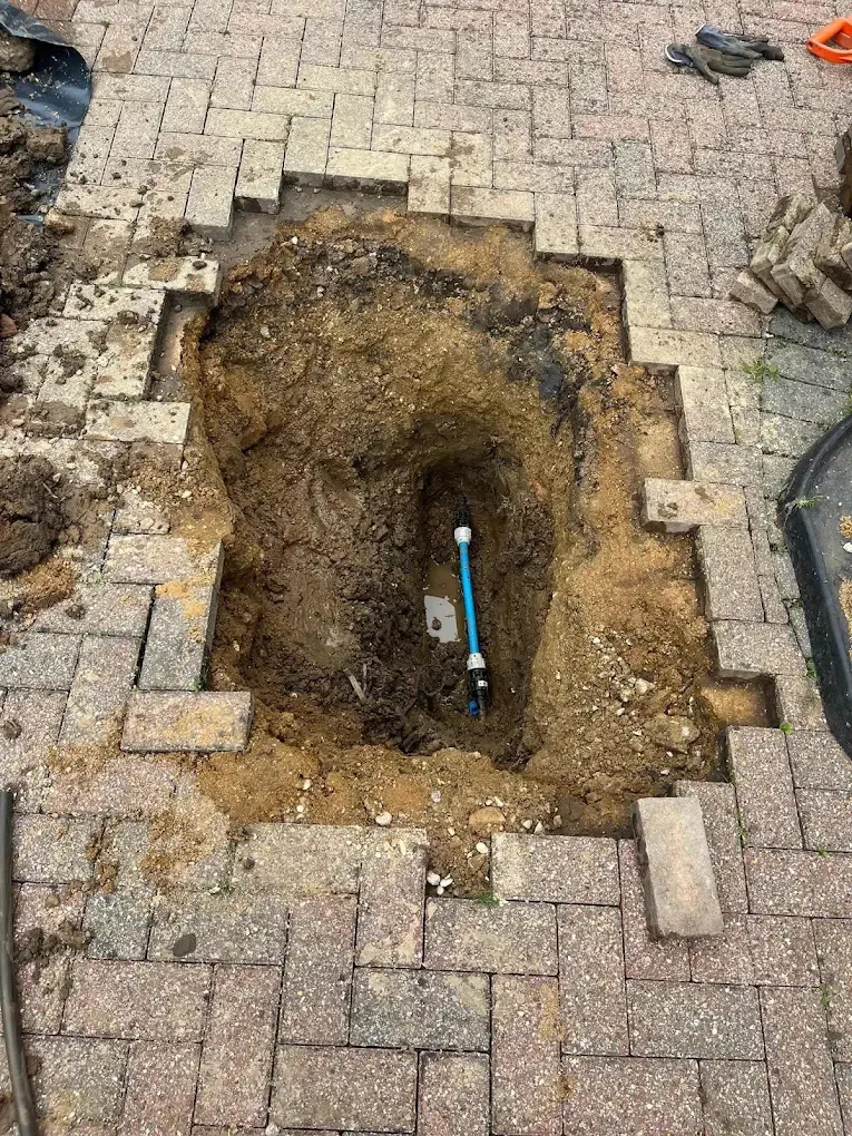 A square of block paving lifted from a drive and a pit dug below it to reach a leaking supply pipe