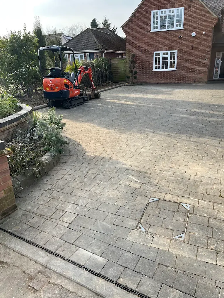 An orange micro digger parked on a block paved drive in front of a detached brick house