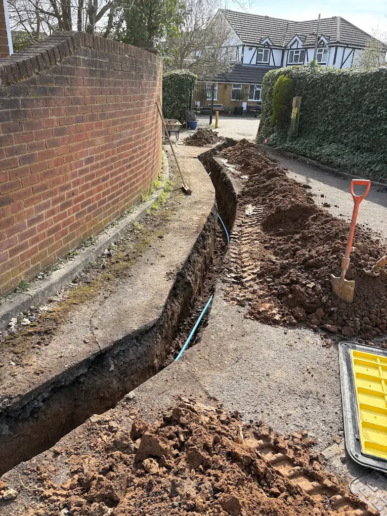 A trench running the length of a shared driveway with the spoil banked neatly alongside it