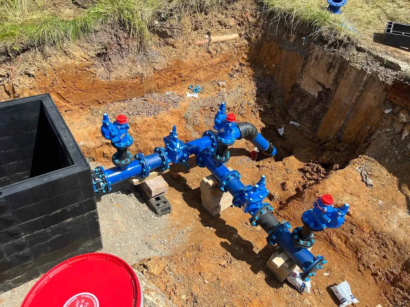 A row of blue valves and fittings laid out in an open excavation, splitting one connection into several new supplies