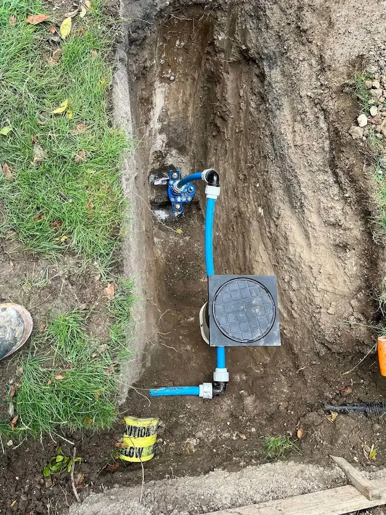 A trench cut through a lawn with a new stop tap fitting and boundary box set in at one end