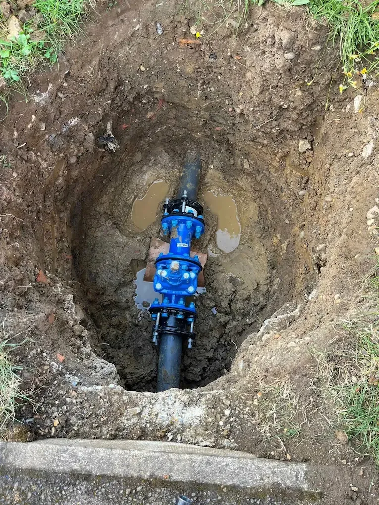 A round pit with water at the bottom and a blue meter fitting connected on a black pipe