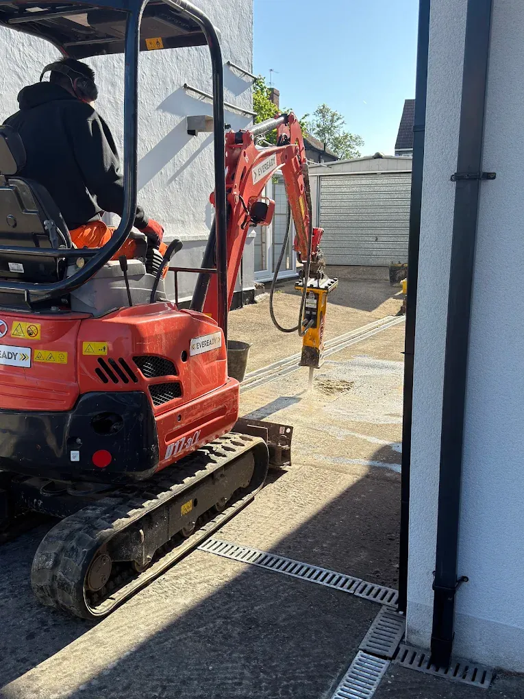 An operator in a micro digger working down a narrow side passage beside a house