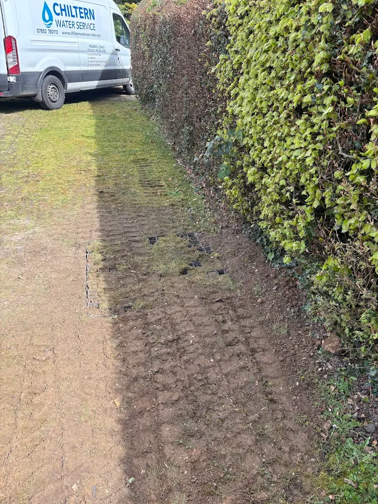 A strip of reinstated ground along a hedge line across a lawn, with the Chiltern Water Services van parked beyond